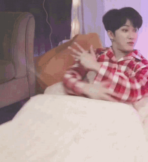 a young man in a plaid shirt is sitting on a bed
