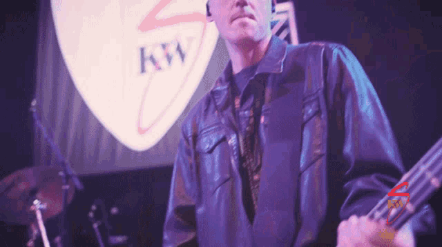 a man playing a bass guitar in front of a kw logo