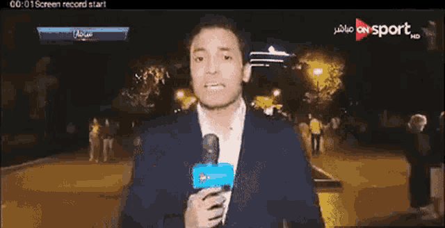 a man in a suit is holding a microphone in front of a screen that says ' on sport ' on it