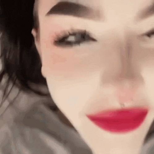 a close up of a woman 's face with red lipstick and a nose piercing .
