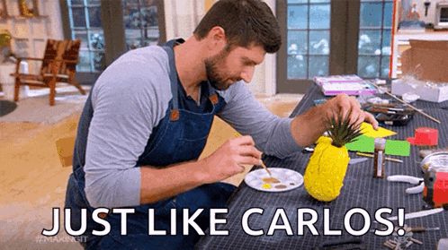 a man is sitting at a table painting a pineapple with the words just like carlos .
