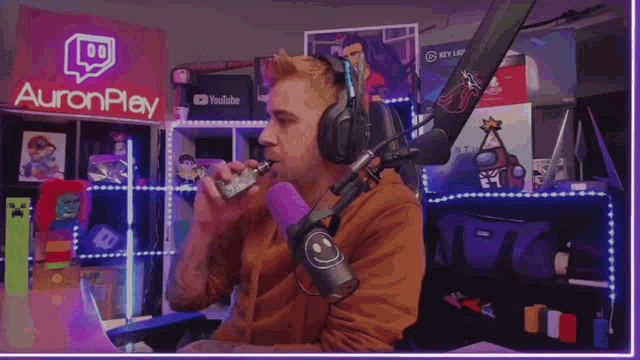 a man wearing headphones is smoking an electronic cigarette in front of a sign that says auron play