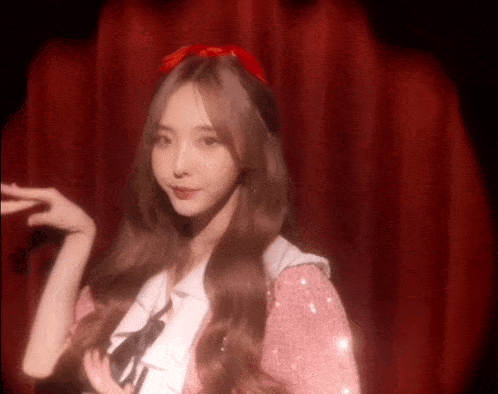 a woman in a pink dress with a red bow on her head stands in front of a red curtain