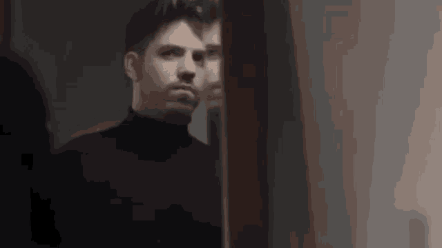 a man in a black turtleneck is looking at his reflection in a mirror .