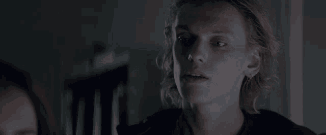 a young man with long blonde hair is looking at something in the dark