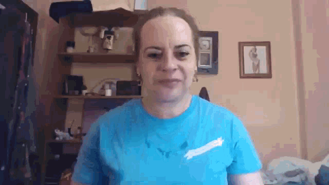 a woman wearing a blue t-shirt is standing in front of a wall with pictures on it .