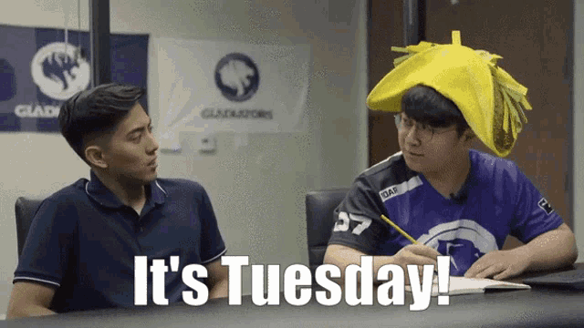two men are sitting at a table with the words it 's tuesday on the bottom