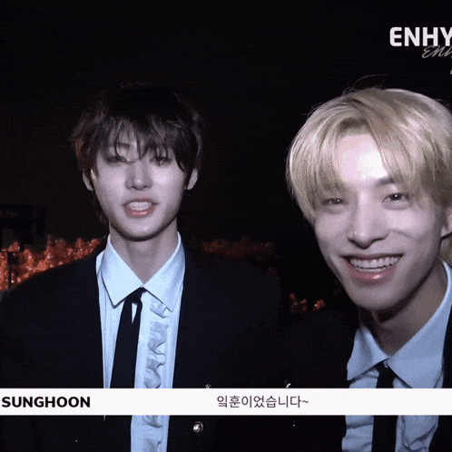 two young men in suits and ties are smiling in front of a sign that says enhy