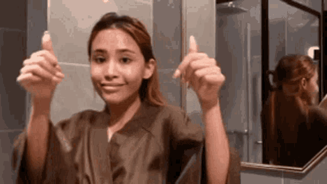 a woman is giving a thumbs up sign in front of a mirror .