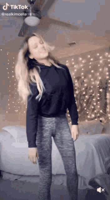 a woman in a black hoodie and grey leggings is dancing in a bedroom with a ceiling fan .