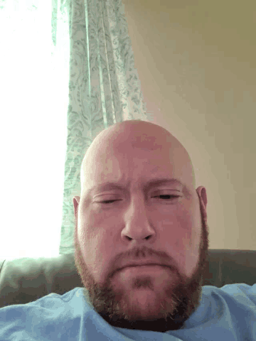 a bald man with a beard laying on his back with his eyes closed