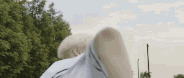 a man with white hair is kicking a soccer ball in a field with trees in the background .