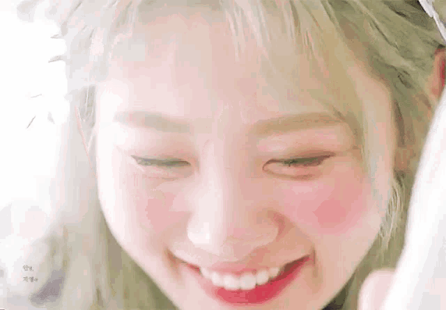 a close up of a woman 's face with pink cheeks and a smile .