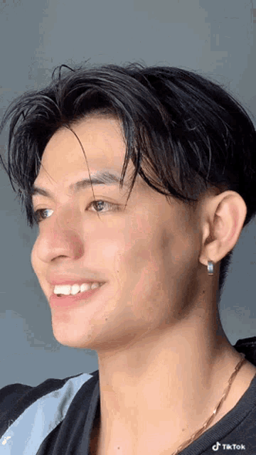 a young man wearing earrings and a necklace is smiling for the camera ..