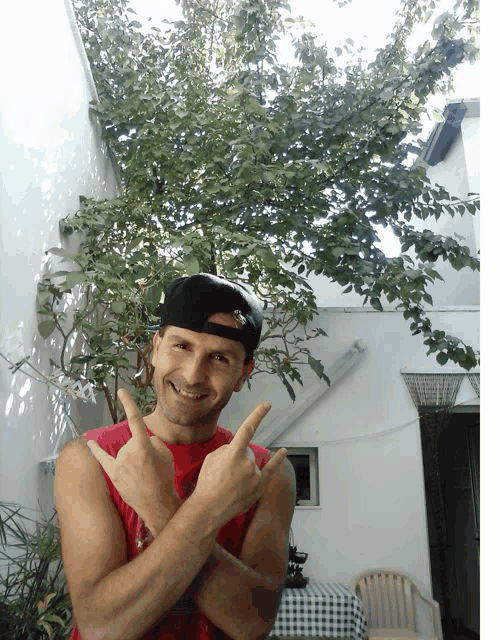 a man wearing a red tank top and a black hat is giving the thumbs up sign