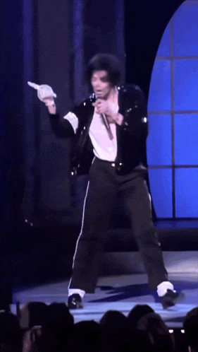 a man in a black jacket and white gloves is singing into a microphone on a stage