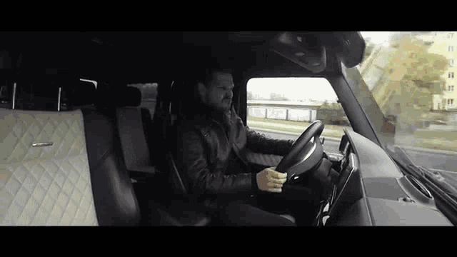 a man is sitting in the driver 's seat of a car holding the steering wheel .