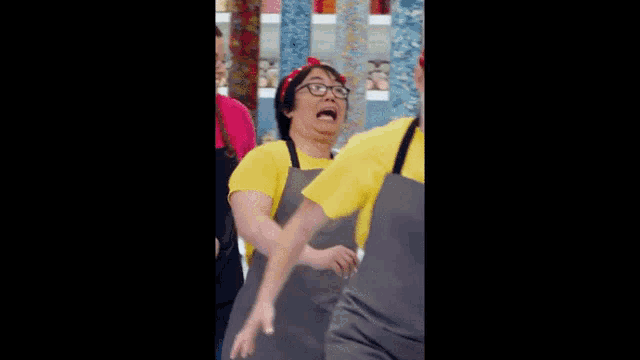 a woman in a yellow shirt and apron is talking to another woman in an apron .