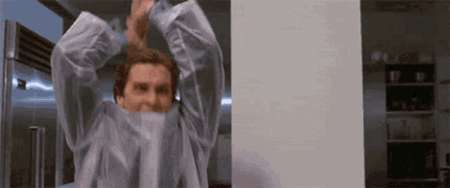a man is covering his face with a plastic sheet while standing in front of a refrigerator .
