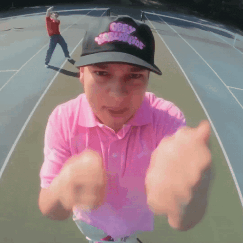 a man wearing a pink shirt and a black hat with obey on it