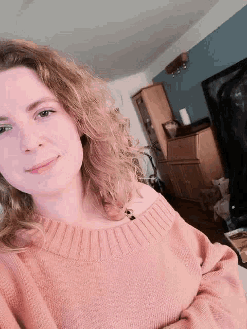a woman in a pink sweater is taking a selfie in a living room