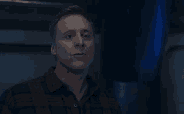 a man in a plaid shirt is standing in a dark room in front of a blue wall .