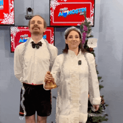 a man and a woman standing in front of a christmas tree with a sign that says radio a nostri