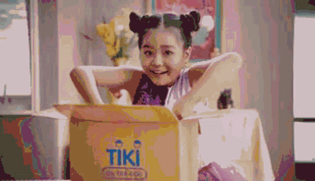 a little girl is sitting in a box that says tiki on it