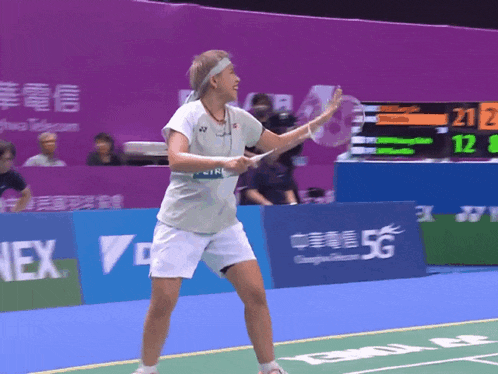 a woman playing badminton on a court with a 5g banner behind her