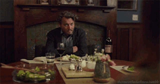 a man is sitting at a table with a glass of wine