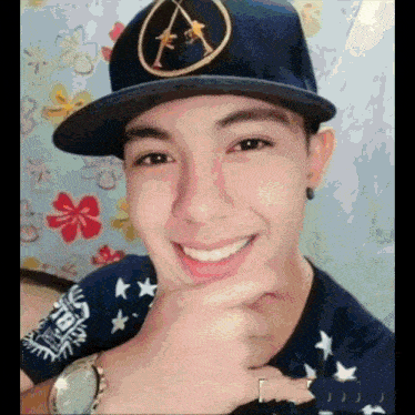 a young man wearing a hat and smiling with his hand on his chin .