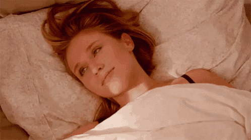 a woman is laying in bed under a blanket with her eyes closed and her hair blowing in the wind .