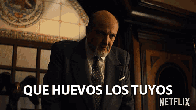 a man in a suit and tie stands in front of a sign that says que huevos los tuyos