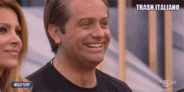 a man in a black shirt is smiling in front of a woman and a sign that says trash italiano on it