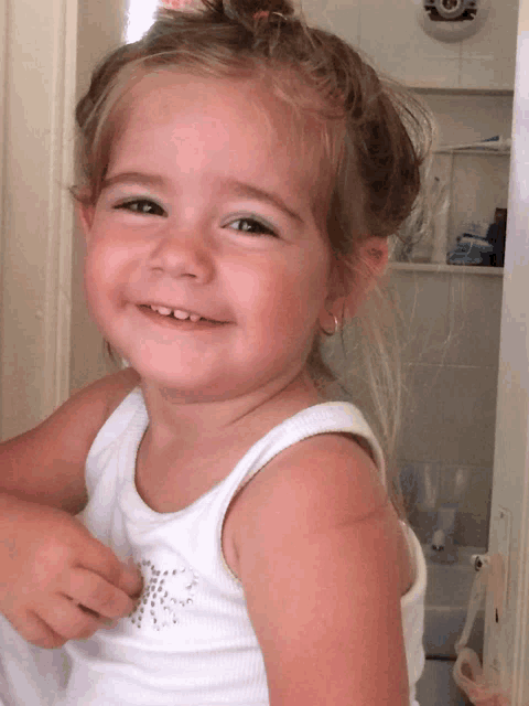 a little girl wearing a white tank top is smiling for the camera