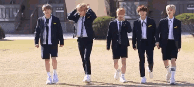 a group of young men in school uniforms are walking across a field .