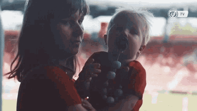 a woman is holding a baby with a pacifier in his mouth and a tv logo on the bottom right