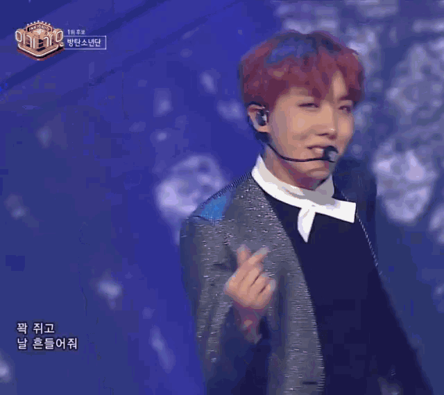 a young man with red hair is making a heart shape with his hands while standing on a stage .