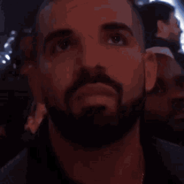 a man with a beard is sitting in a dark room looking up at something .