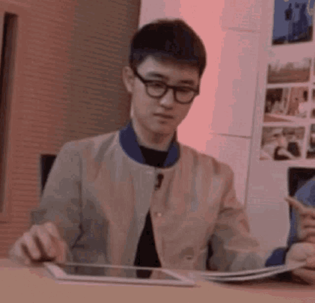 a young man wearing glasses is sitting at a table with a tablet .