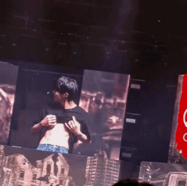 a man taking off his shirt on a stage in front of a large screen
