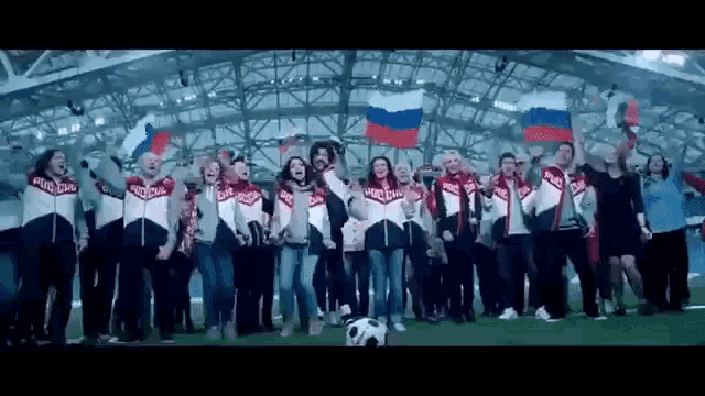 a group of people are standing on a soccer field holding russian flags and a soccer ball .