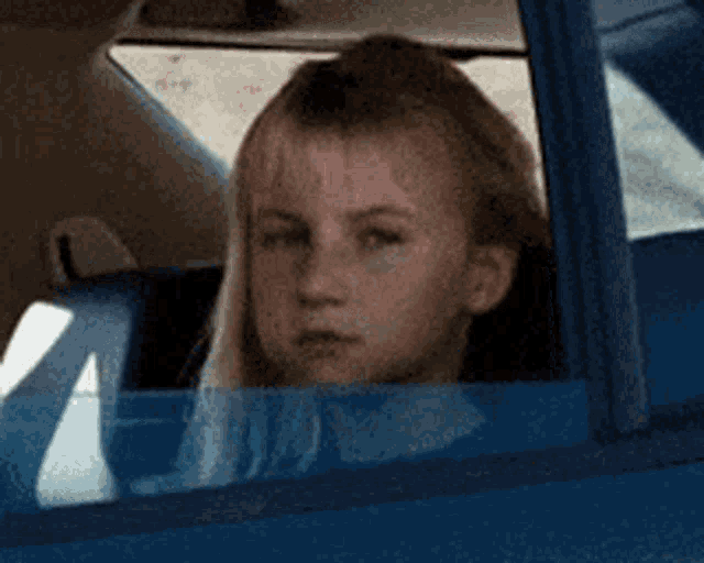 a young girl is looking out of the window of a blue car .