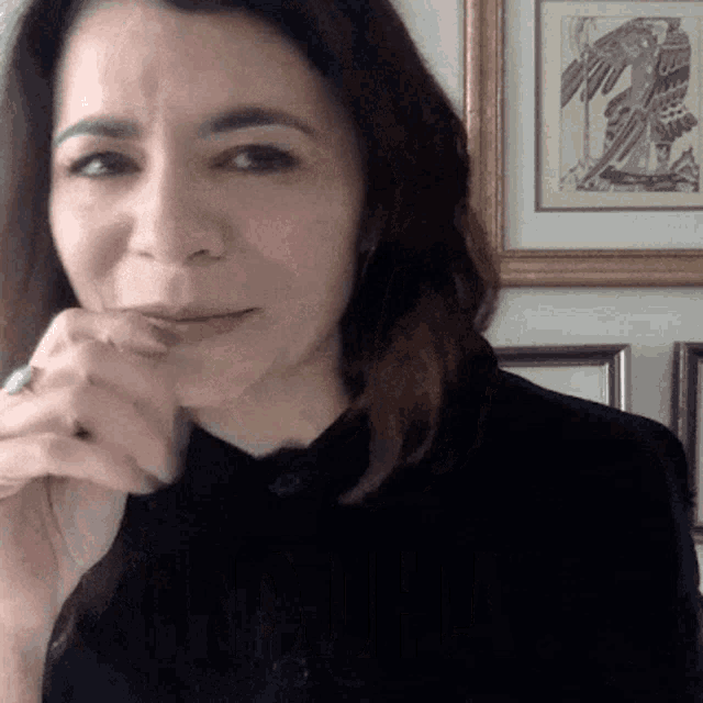 a woman with a ring on her finger looks at the camera with a framed picture in the background