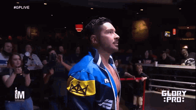 a man in a blue and yellow jacket is holding a microphone in front of a crowd and the words glory pro are on the screen