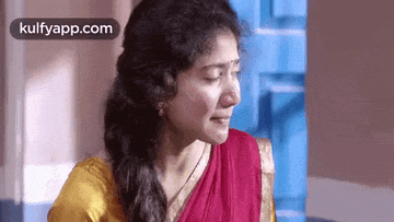 a woman in a red and yellow sari is crying while standing next to a blue door .