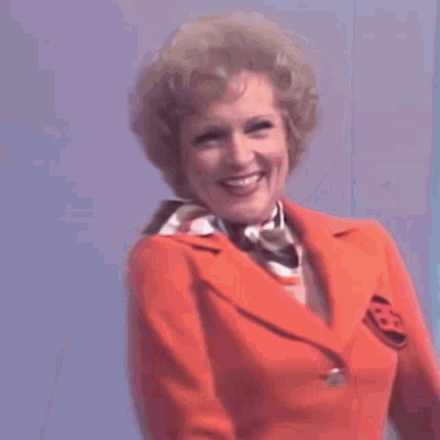 a woman in a red jacket and scarf is smiling and looking at the camera .