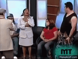 a group of people are sitting in a waiting room and a man is standing in the middle of the room .