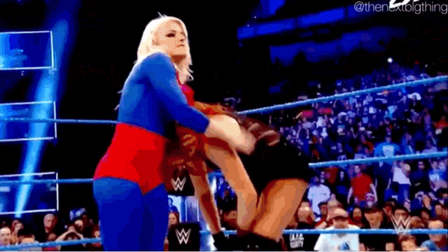 a woman is wrestling another woman in a wrestling ring while a crowd watches .