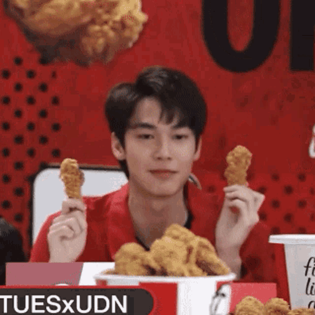 a man holding a fried chicken wing in front of a kfc sign